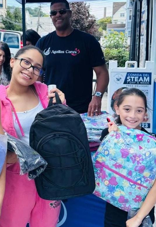 Two students receiving backpacks at an Agallas Cares school supply giveaway